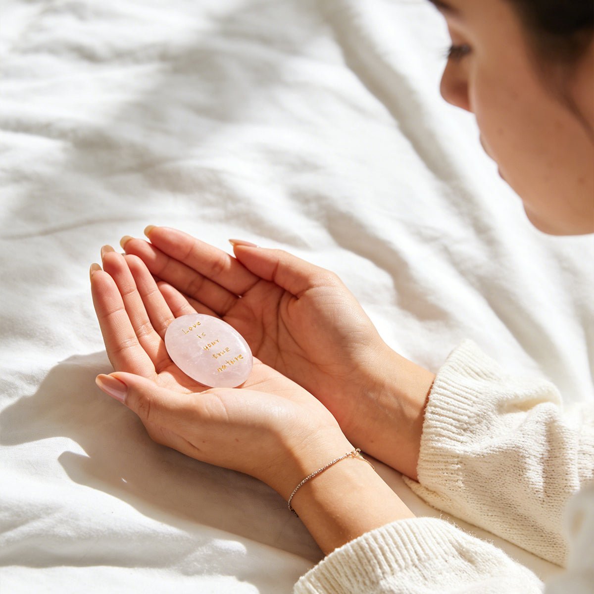 Rose quartz oval stone held in hands on a white blanket