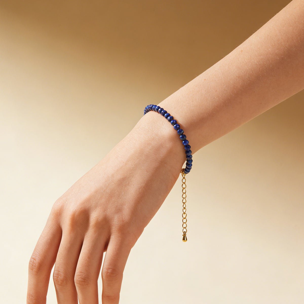 Lapis lazuli bead bracelet on hand with gold-tone chain drop charm