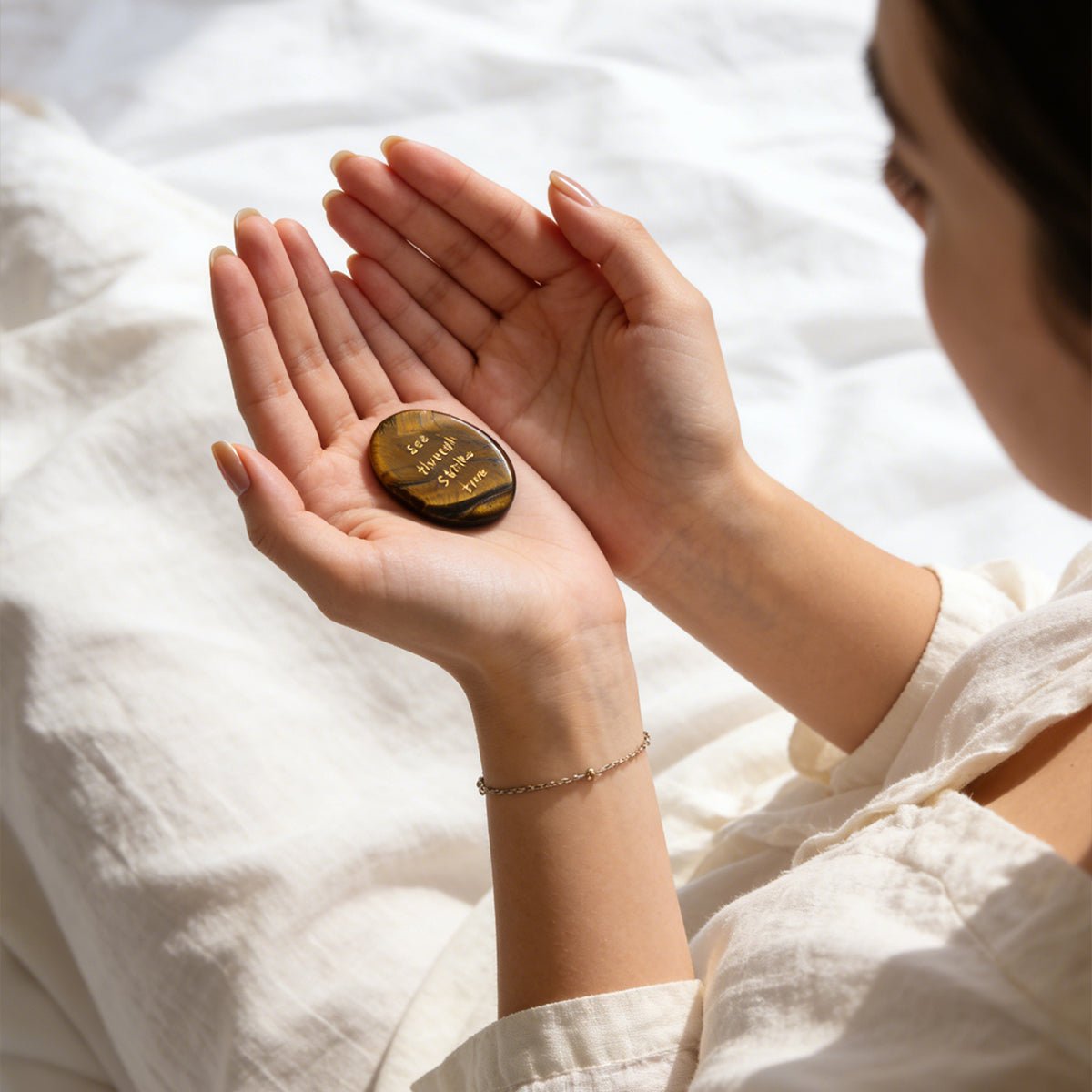 Tiger’s eye stone held in two hands, oval gold-brown with engraved text