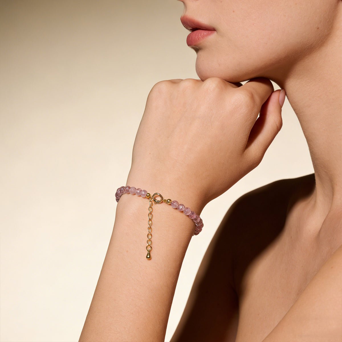 Pink bead bracelet with gold clasp and long dangling charm on forearm