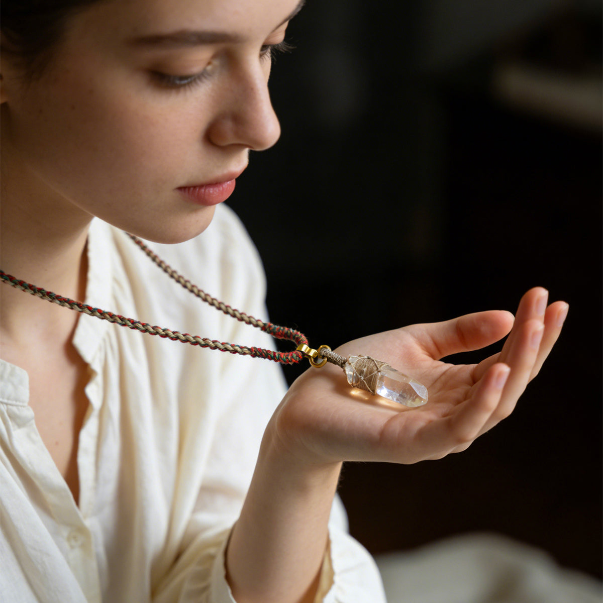 Quartz point pendant necklace held near chest; gold tone bail and wire-wrapped crystal point