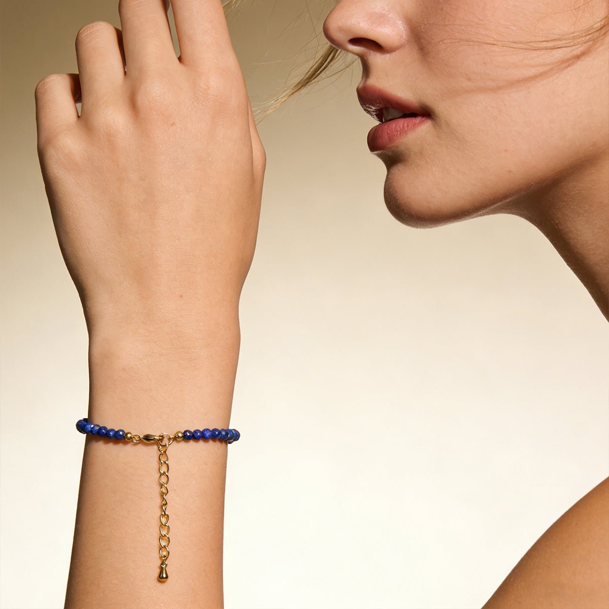 Lapis lazuli bead bracelet on wrist with gold-tone dangling chain charm