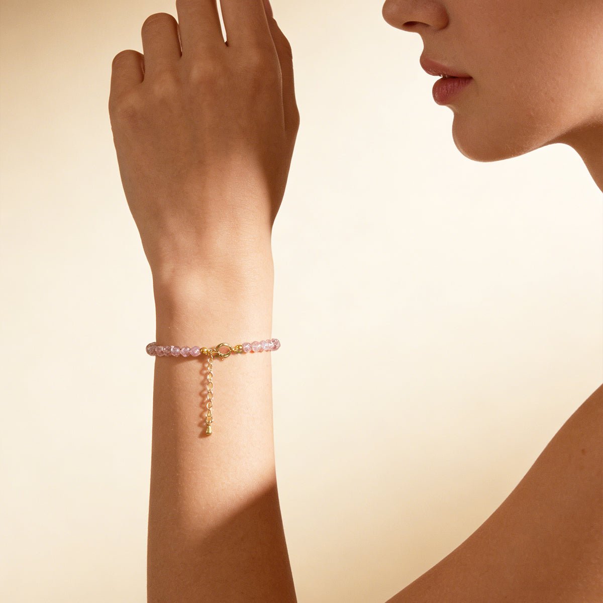 Pink quartz bead bracelet with gold clasp and dangling charm on wrist