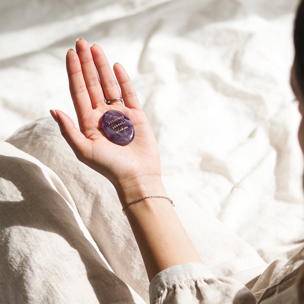 Amethyst oval stone resting on open palm, gold 'Stillness reveals wisdom' inscription