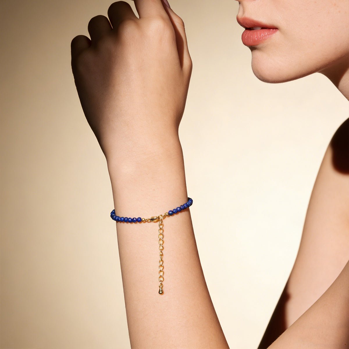 Lapis lazuli bead bracelet on wrist with gold-tone dangling chain charm