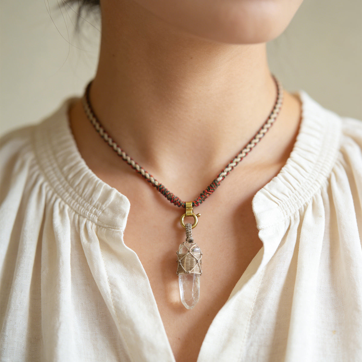 Quartz point pendant necklace worn at neckline with gold tone ring bail and wire wrap