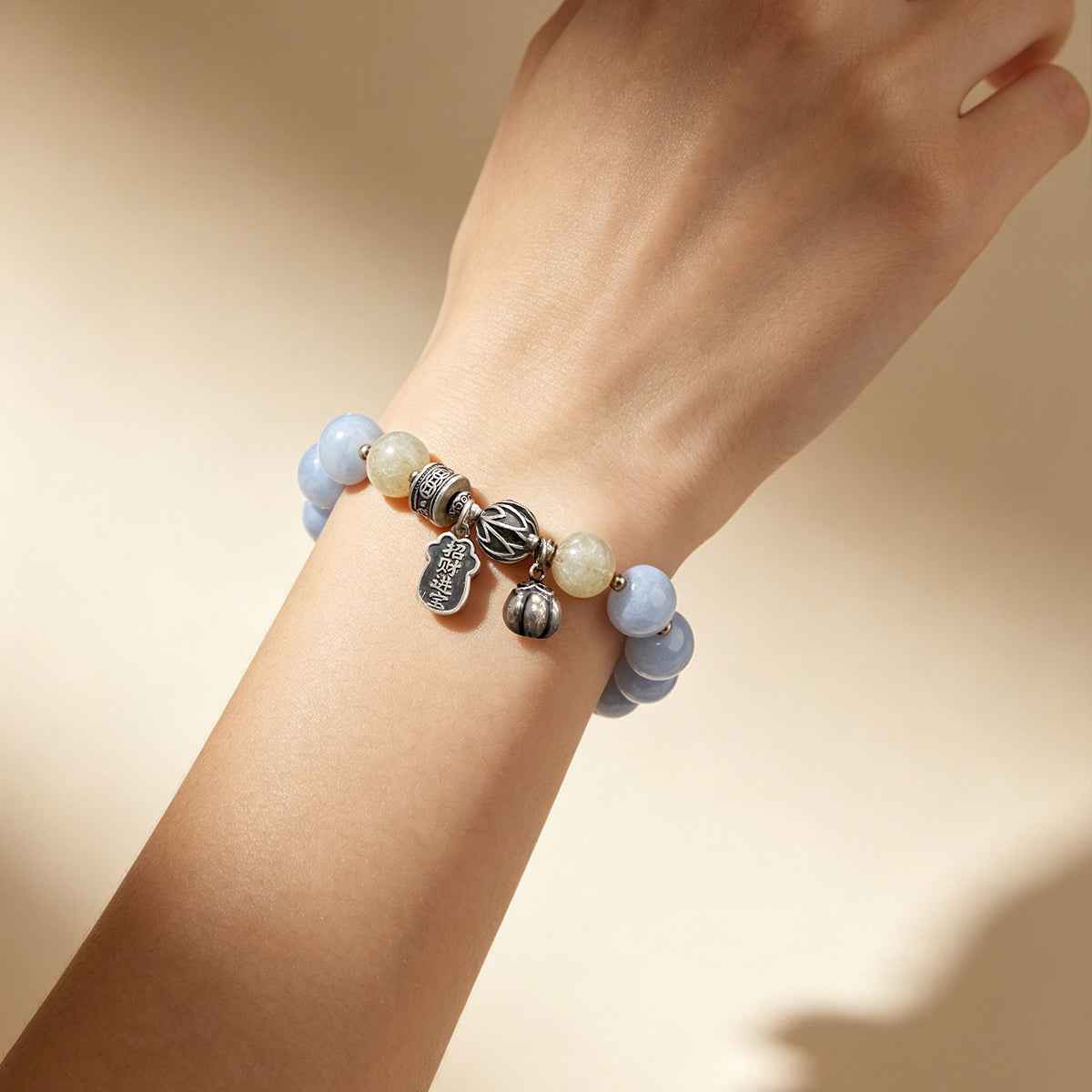 Light-blue bead charm bracelet with silver-tone charms on wrist and pale green beads