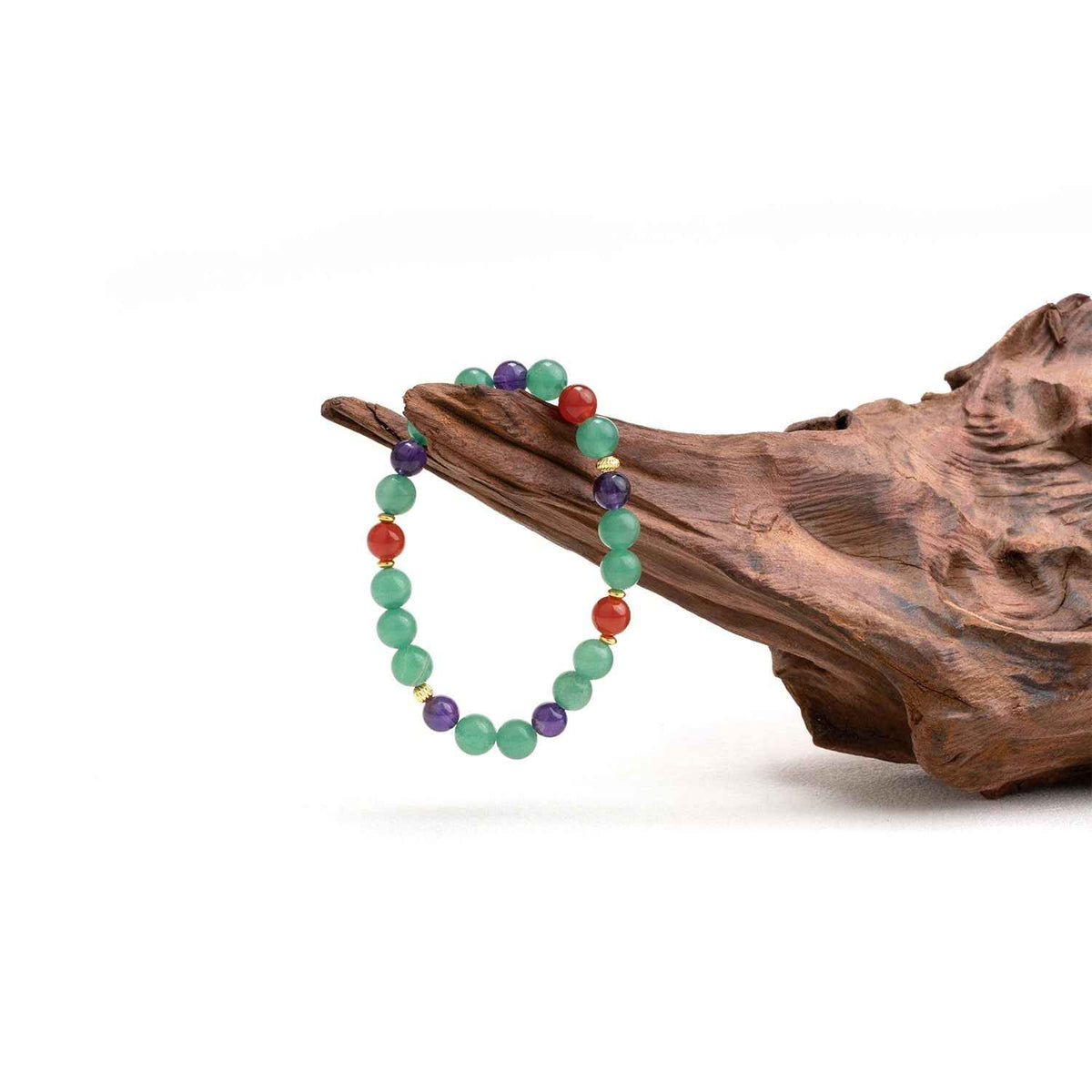 Crystal bead bracelet with green, purple, and red stones on driftwood