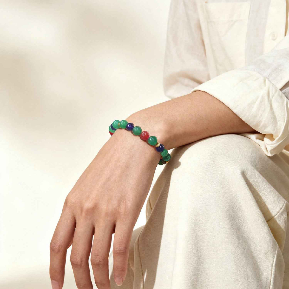 Crystal bead bracelet on wrist with green, purple, and red beads and gold-tone spacers