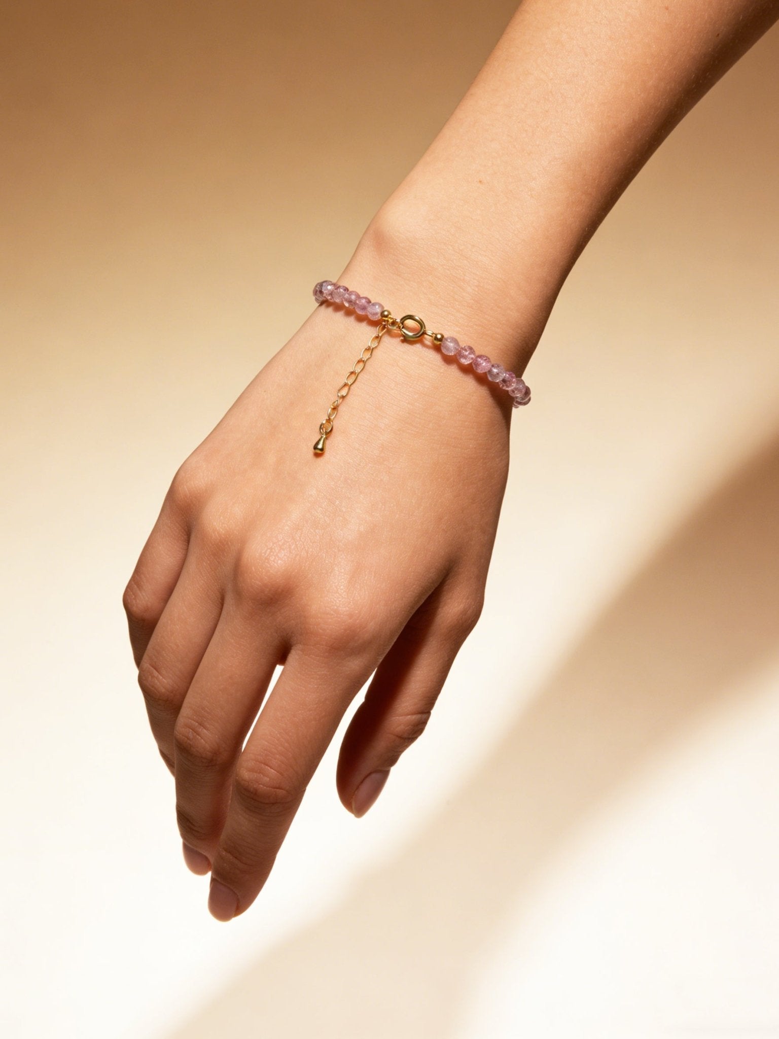 Pink bead bracelet with gold clasp and hanging tassel charm on wrist
