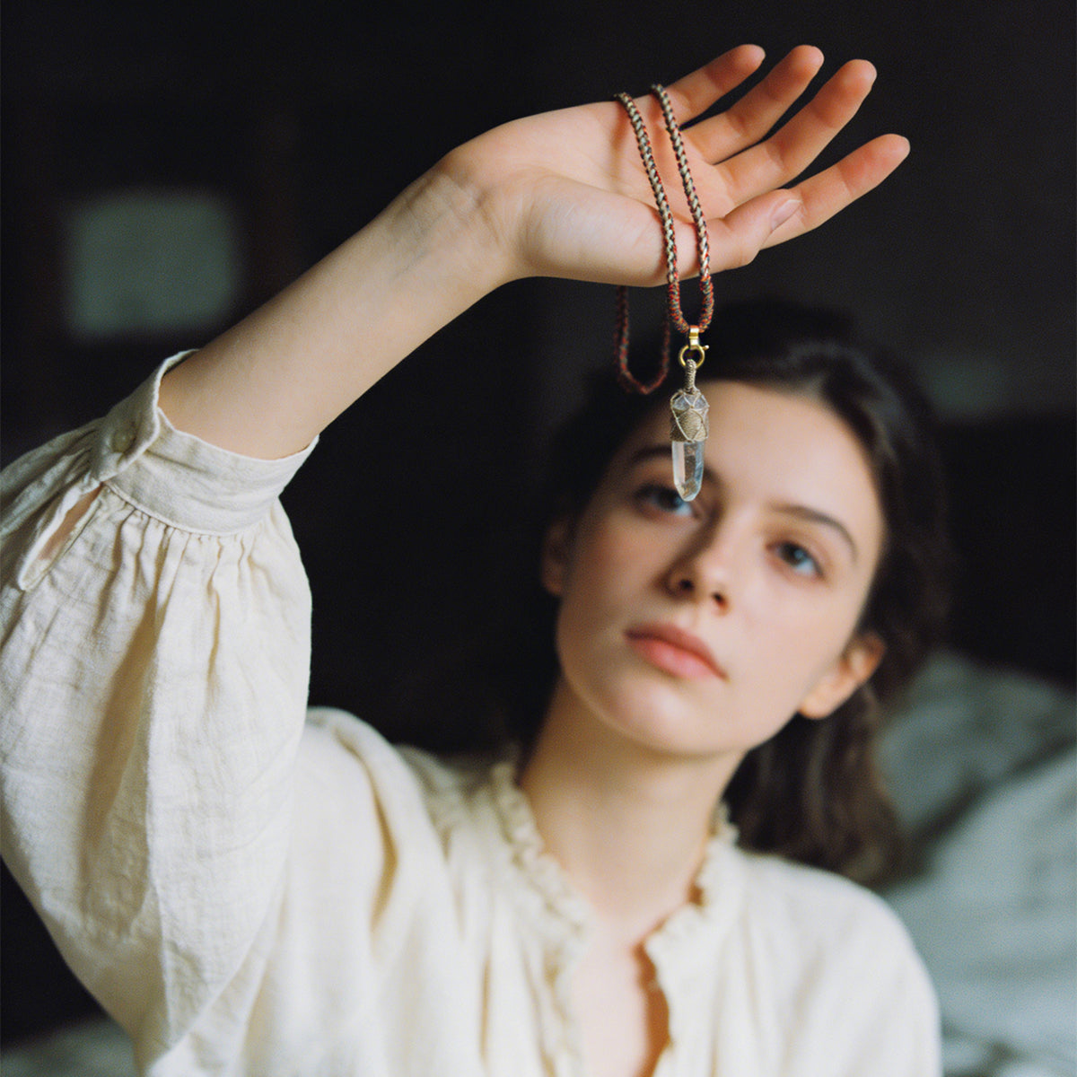 Quartz point pendant necklace resting in hand; beaded cord with gold tone ring bail