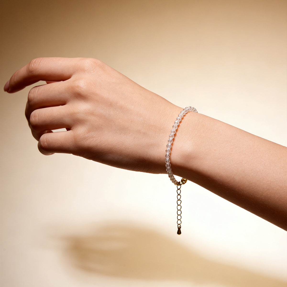 Clear quartz bead bracelet worn on wrist with gold dangling charm