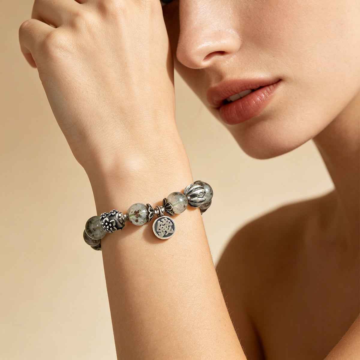 Gray stone beaded bracelet with round silver charm medallion on wrist