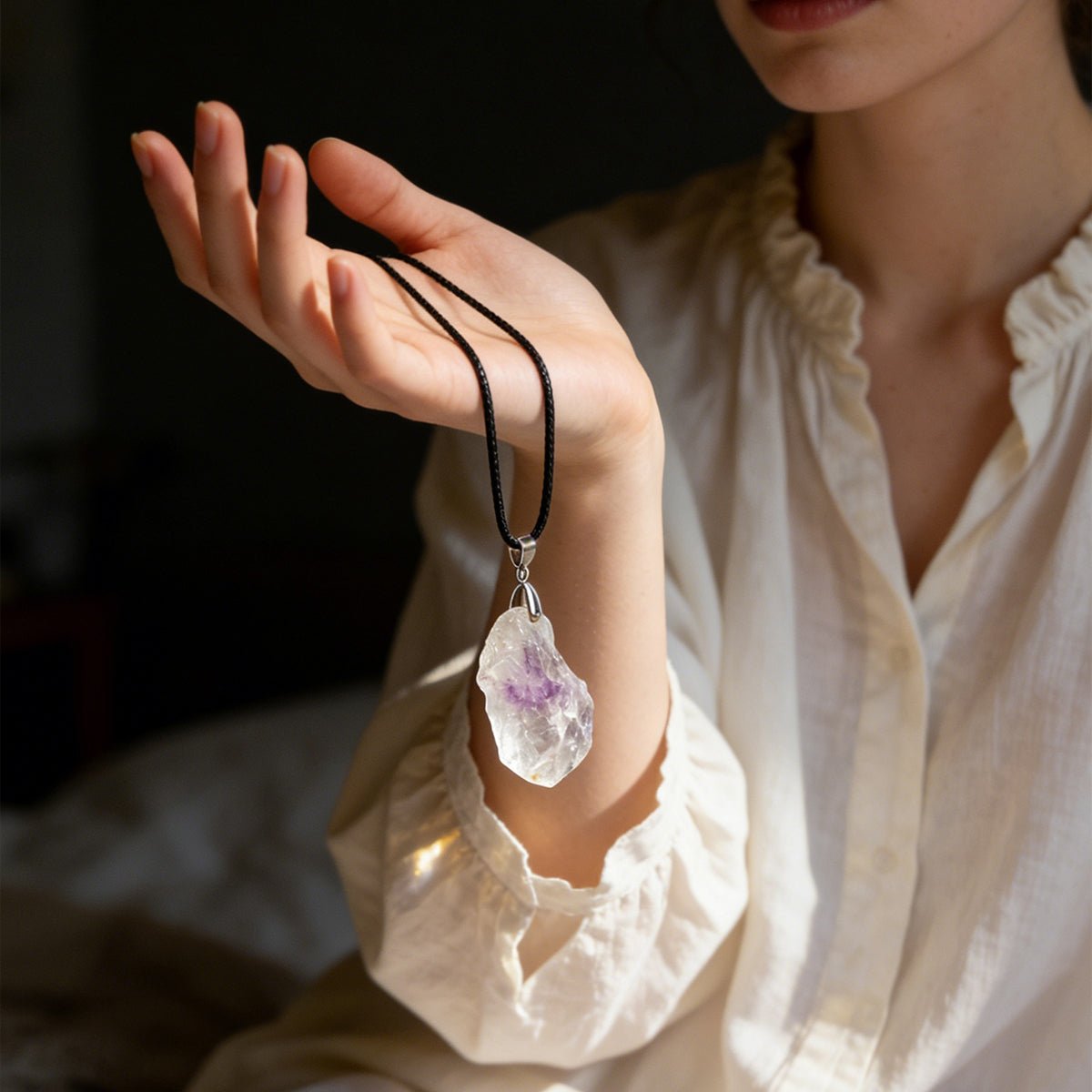 Quartz pendant necklace on black cord, hanging from a person’s wrist