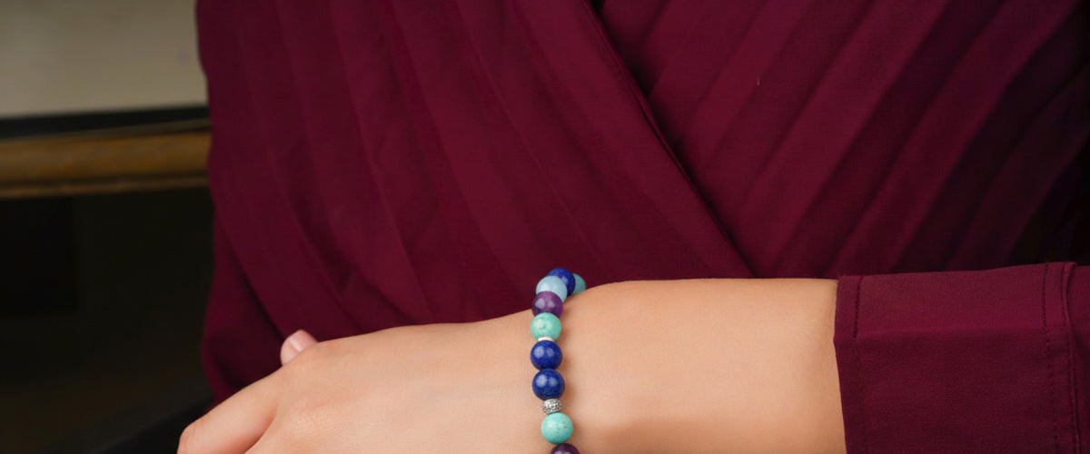 Close-up of a model wearing a multi-gemstone bracelet against a deep burgundy red shirt.