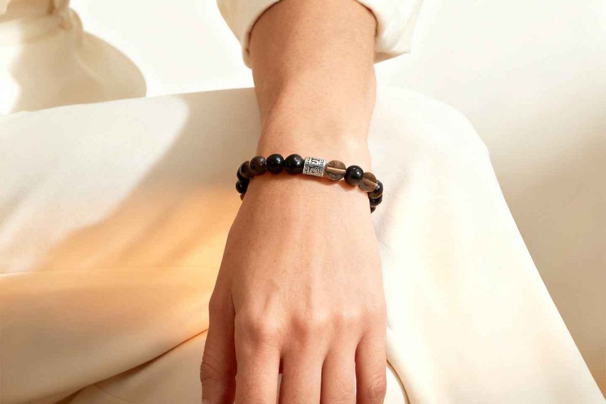 Woman wearing Amesha Energy Root Chakra Guardian Crystal Bracelet - Natural Obsidian and Snowflake Obsidian beads for protection and stability