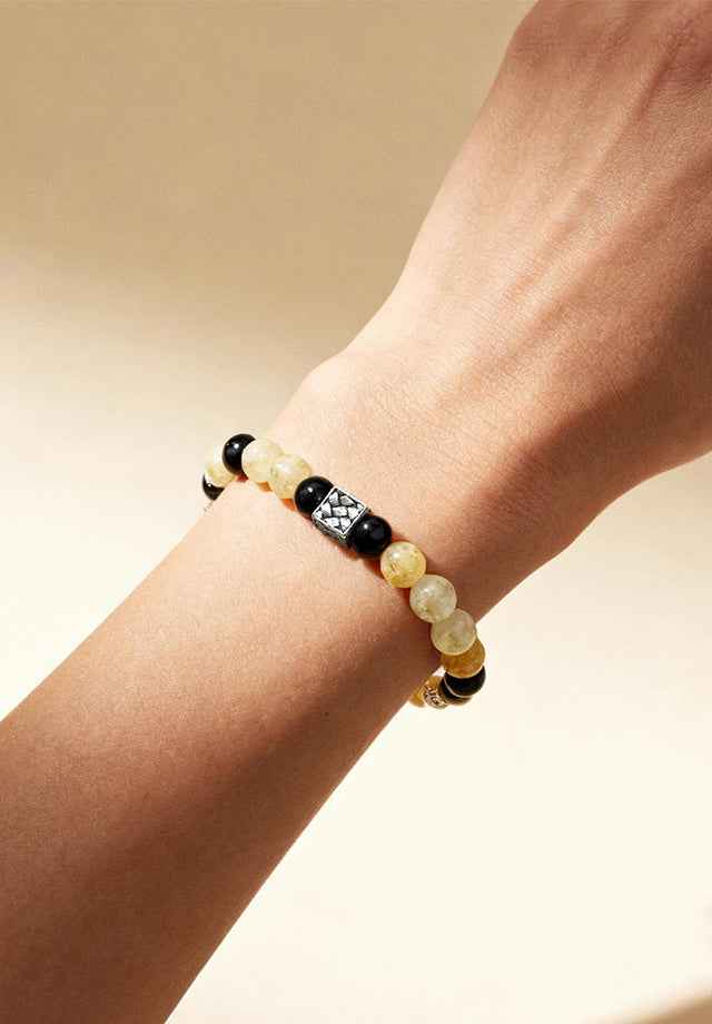 Detail view of wrist wearing Amesha Energy Solar Plexus Bracelet - Natural yellow and black beads with intricate silver charm