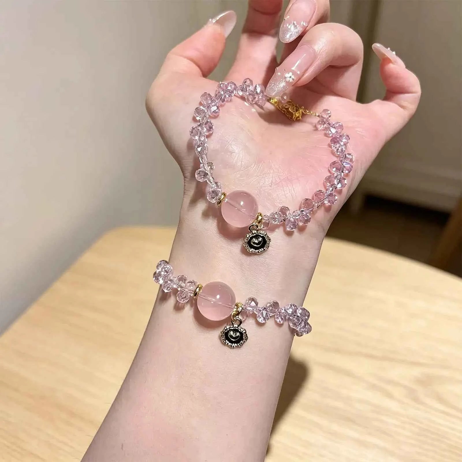 Pink gemstone bracelet worn on wrist with evil-eye charm and dangling bead accents