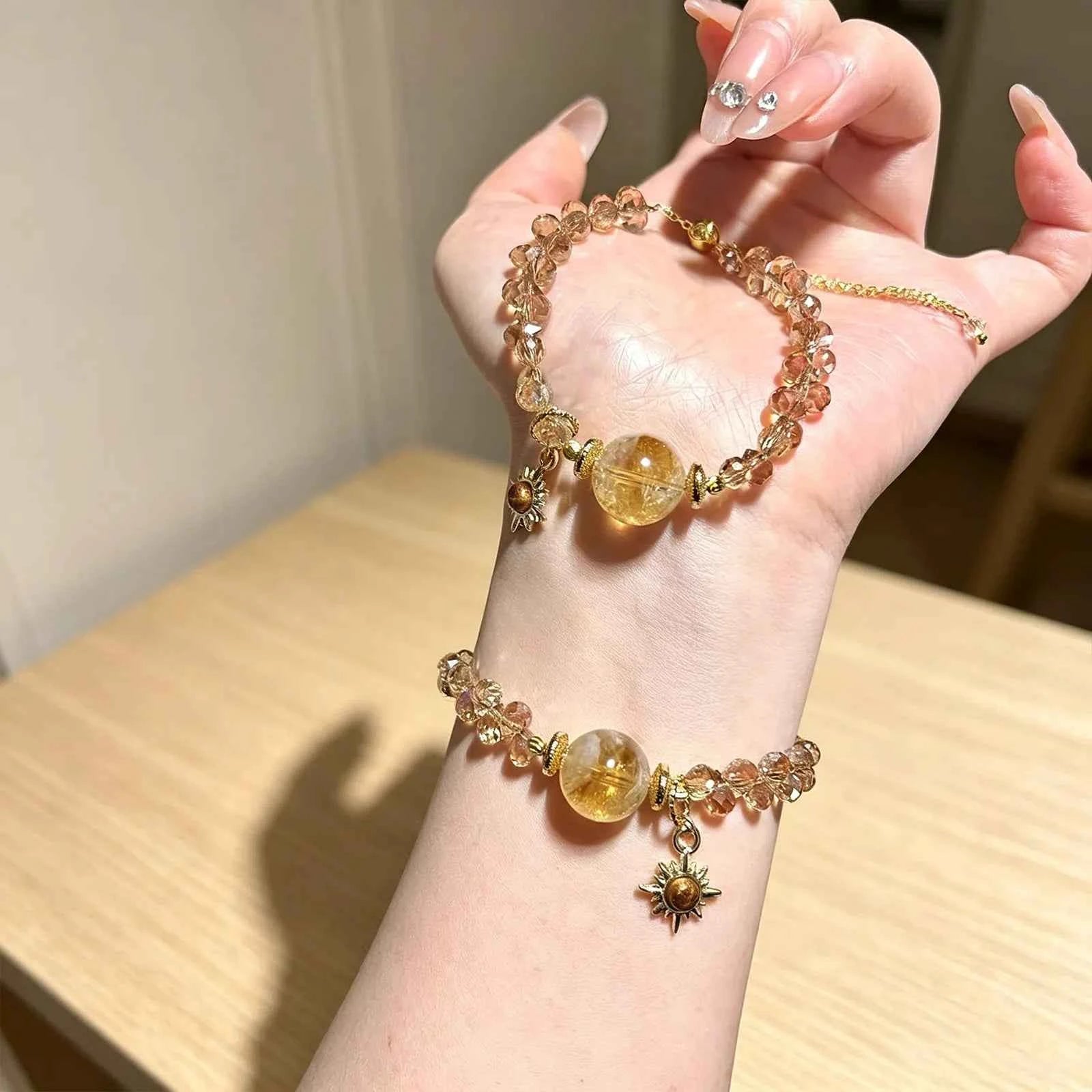 Gold-tone bead bracelet on wrist with round amber quartz pendant and sun charm